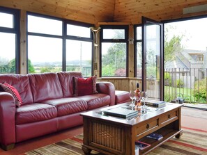A room with a red leather sofa, a wooden coffee table with books and glasses, and large windows offering a view of the outdoors. - 3 bedroom accommodation in Stonehaven (Stonehaven)