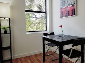 A room with a wooden floor, a black table with a chair, a potted plant, a window with a view of trees, and a framed picture on the wall. - Cute and Cozy 1-Brm Apt in the Heart of Miami!! #11 (Miami)