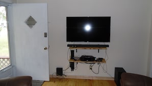 Un salon doté d’un téléviseur à écran plat fixé au mur, d’un parquet et de deux fauteuils en cuir.