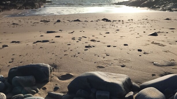 Una spiaggia con rocce sparse, impronte, cielo sereno e l'oceano sullo sfondo.