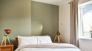 Una camera da letto con un letto, due comodini, una finestra con tende e una parete decorata con un tocco di verde.