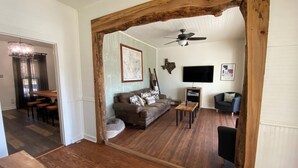 A spacious living area with a wooden floor, a ceiling fan, a sofa, a TV, and a dining area with a table and chairs. - The Lodge on Salado Creek includes golf cart (Salado)