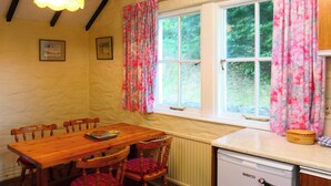 A kitchen with a wooden table, chairs, a refrigerator, and a window with floral curtains.