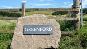 A stone sign with the name "GREENFORD" in a rural setting with a wooden fence, greenery, and a clear sky. - 3 bedroom accommodation in Dundee (Dundee)