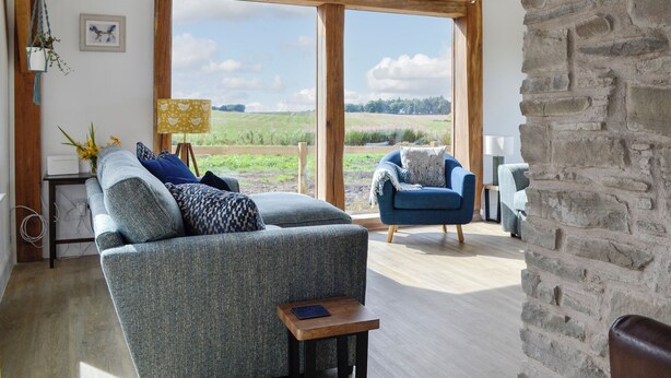 A spacious living room with a large window, a blue sofa, a wooden coffee table, and a view of a green field. - 3 bedroom accommodation in Dundee (Dundee)