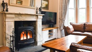 Una sala de estar con chimenea, televisor, sofá y ventana con cortinas.