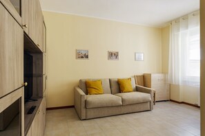Een woonkamer met een bank, een kast met een televisie en een raam met gordijnen.