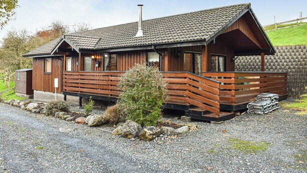 Une cabane en bois avec un toit en pente, une cheminée et une véranda dotée de balustrades en bois.