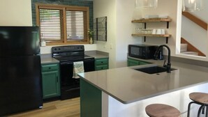A kitchen with green cabinets, a black refrigerator, a microwave, and a large island with stools. - REMODELED! 2B/2B, Deck off10th GOLF Green, Dog Friendly, Pool, WIFI, in Resort! (Galena)
