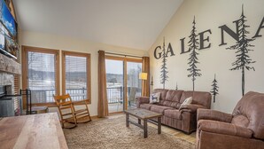 A living room with a brown leather sofa, a wooden coffee table, and a large window with blinds. - REMODELED! 2B/2B, Deck off10th GOLF Green, Dog Friendly, Pool, WIFI, in Resort! (Galena)