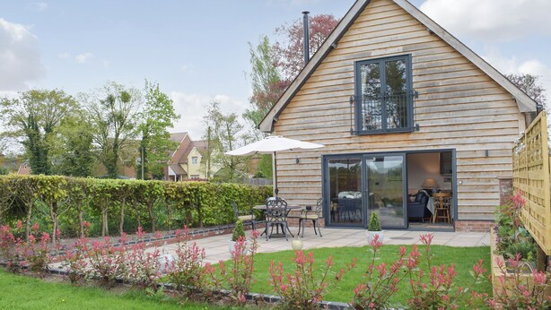 Una casa in legno con un'ampia porta finestra, un patio con mobili da esterno e un giardino curato.