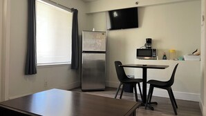 Uma cozinha compacta com geladeira, micro-ondas e TV de tela plana fixada na parede.