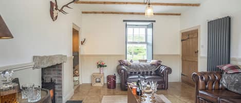 A rustic living room with exposed wooden beams, a fireplace, leather sofas, and a wooden coffee table.