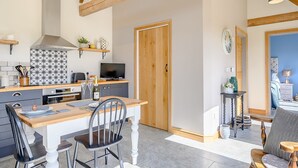 A modern kitchen with a dining area, wooden beams, a TV, and a door leading to a bedroom.
