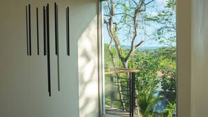 A room with a large window overlooking a lush landscape, a wooden staircase, and a wall with vertical black lines. - 2BR, 2.5BA, Jungle views, walk to beach, Pool, AC (Nicoya)