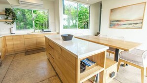 A modern kitchen with wooden cabinets, a white countertop, and a large window offering a view of greenery. - 2BR, 2.5BA, Jungle views, walk to beach, Pool, AC (Nicoya)