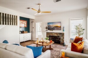 Un salon avec une cheminée, un téléviseur et un ventilateur de plafond.