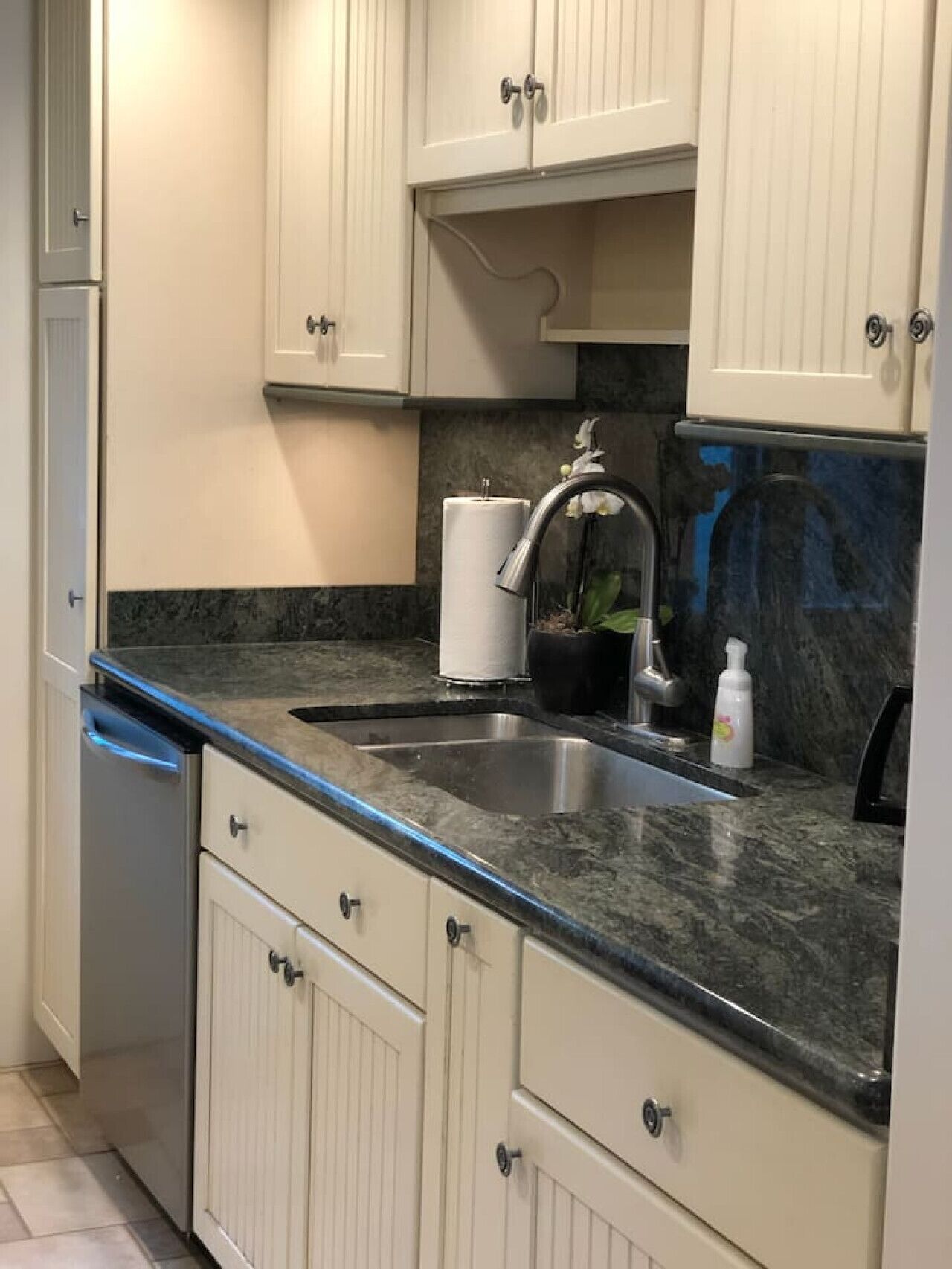 Una cocina con gabinetes blancos, un lavamanos de acero inoxidable, encimera de mármol y escurreplatos.