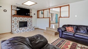 A living room with a fireplace, a leather sofa, and a television mounted on the wall. - 5 min  to Old Town - Prime location - Game Room - gated parking  (Albuquerque)