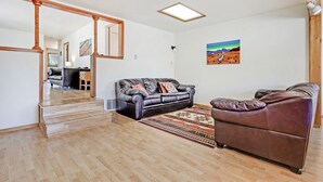 A spacious living room with a brown leather sofa, a black leather sofa, a wooden staircase, and a painting on the wall. - 5 min  to Old Town - Prime location - Game Room - gated parking  (Albuquerque)