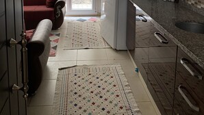 Eine kompakte Küche mit Kühlschrank, Mikrowelle und Spüle. Im Wohnbereich befindet sich ein rotes Sofa und ein gemustertes Teppich.