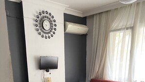 Ein Wohnzimmer mit einem roten Sofa, einem Fernseher, einer Wanduhr und einem gemusterten Teppich.