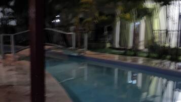 A swimming pool with a stone deck, surrounded by greenery and a building with balconies.
