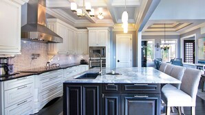 Una cocina amplia con una isla grande, armarios blancos y electrodomésticos modernos.