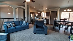 Un salon spacieux avec un canapé bleu, un fauteuil gris et un coin repas comprenant une table et des chaises.