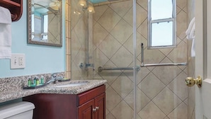 Un bagno con doccia, un lavabo con piano in granito, uno specchio e una finestra.