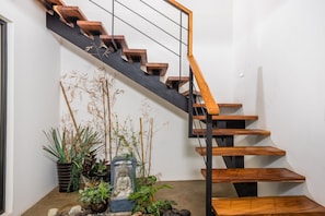 A modern staircase with wooden steps and a black railing, surrounded by potted plants and a stone Buddha statue.