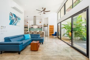 A modern living room with a blue sectional sofa, a wooden coffee table, and a large glass door leading to a balcony with plants.