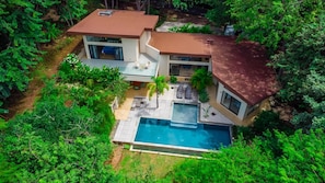 A modern two-story house with a swimming pool, surrounded by lush greenery.