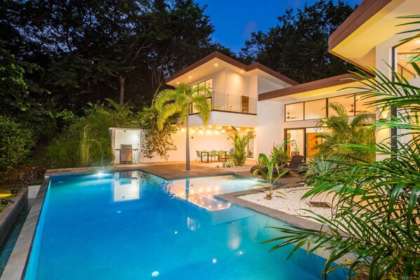 A modern house with a swimming pool, surrounded by lush greenery and trees.