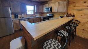 Une cuisine moderne avec des meubles en bois, un réfrigérateur en acier inoxydable, un four à micro-ondes et une cuisinière à gaz. On y trouve également des tabourets de bar et un comptoir en bois.