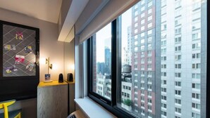 A hotel room with a large window, a radiator, a yellow chair, and a wall-mounted artwork. - Pestana CR7 Times Square (New York)