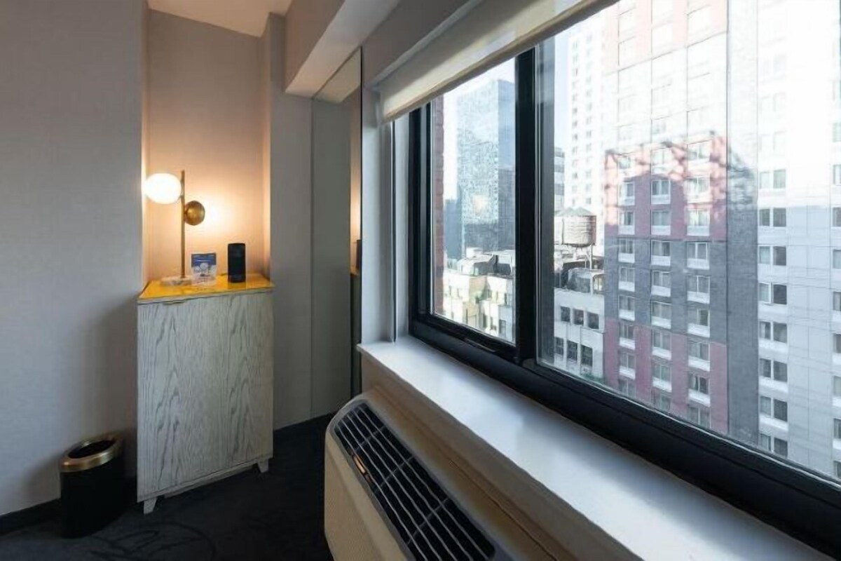 Una habitación de hotel con un ventanal grande, un radiador y una mesita con una lámpara.