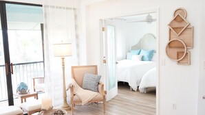 A spacious living room with a large window, a wooden coffee table, a sofa, and a hanging light fixture. - 🏖️Just Remodeled! The Ocean Cottage at Ocean Village Beach Condo (Fort Pierce)