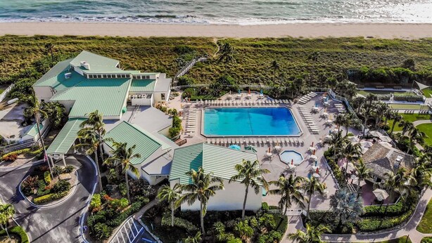 An aerial view of a resort with a large swimming pool, multiple buildings, and a beach in the background. - 🏖️Just Remodeled! The Ocean Cottage at Ocean Village Beach Condo (Fort Pierce)