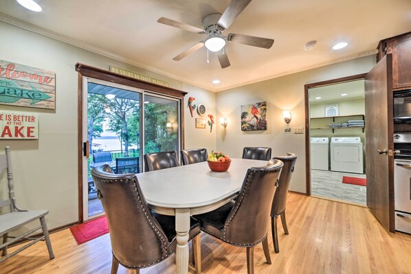 A dining area with a round table, six chairs, a ceiling fan, and a view of a laundry room through an open door.