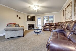 A living room with a fireplace, leather sofas, a glass coffee table, and a ceiling fan.