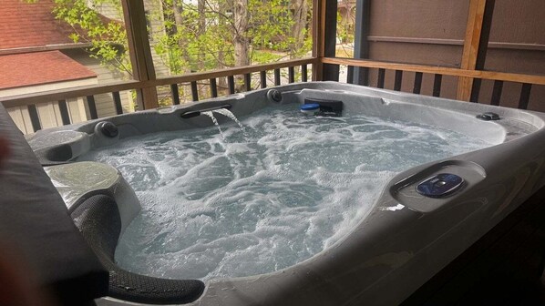 A hot tub with a wooden deck and a view of trees and a building.