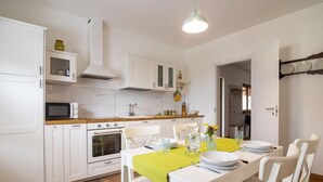 A modern kitchen with white cabinetry, a microwave, an oven, and a dining area with a table set for two. - Casa di Nonno by Interhome (Cividale)