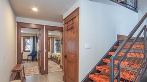 Un pasillo con un banco de madera, una cama con colcha estampada y una escalera de madera con barandales de metal.