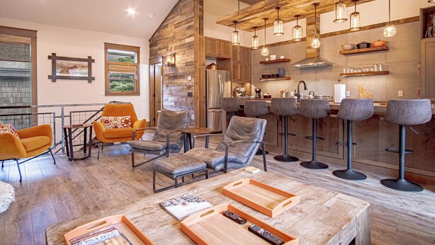Un amplio salón con techo alto, vigas de madera y modernos taburetes de bar.