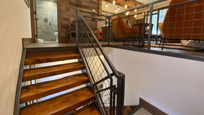 Una escalera de madera con barandillas metálicas que conduce a un segundo piso con vista a una habitación con sillas anaranjadas.