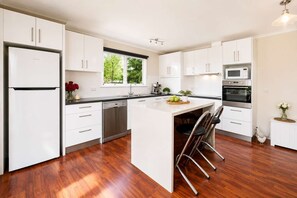 A modern kitchen with white cabinetry, a central island, and a built-in oven. - Historic Baker’s Cottage-Walk to Richmond Village (Richmond)