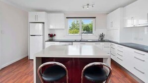 A modern kitchen with white cabinets, a central island, and two bar stools. - Historic Baker’s Cottage-Walk to Richmond Village (Richmond)