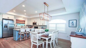 A modern kitchen with white cabinetry, a stainless steel refrigerator, and a dining area with white chairs and a wooden table. - Sanibel Surfsound Home - Heated pool and easy walk to the beach (Sanibel)