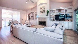 A spacious living room with a large sofa, a fireplace, and a television. - Sanibel Surfsound Home - Heated pool and easy walk to the beach (Sanibel)
